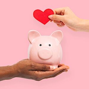 a hand holding a heart over a piggy bank