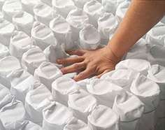 a person's hand on a pile of pocket coils for a mattress support layer