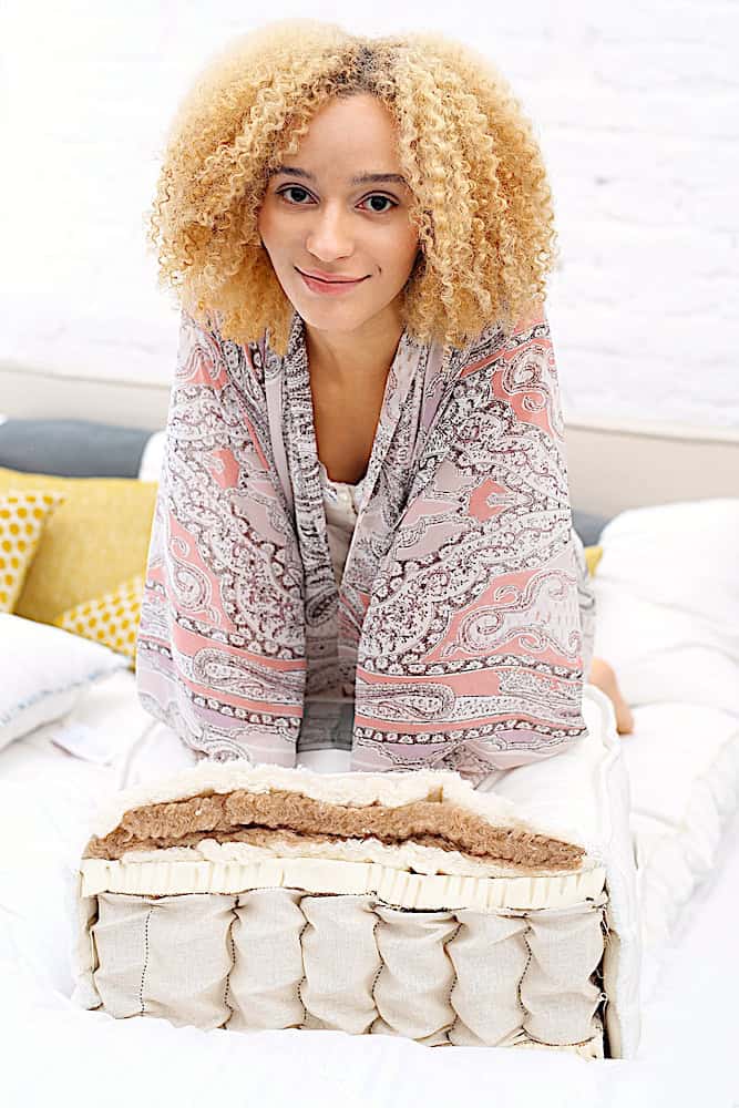 a woman with curly blonde hair showing a cutaway of a mattress
