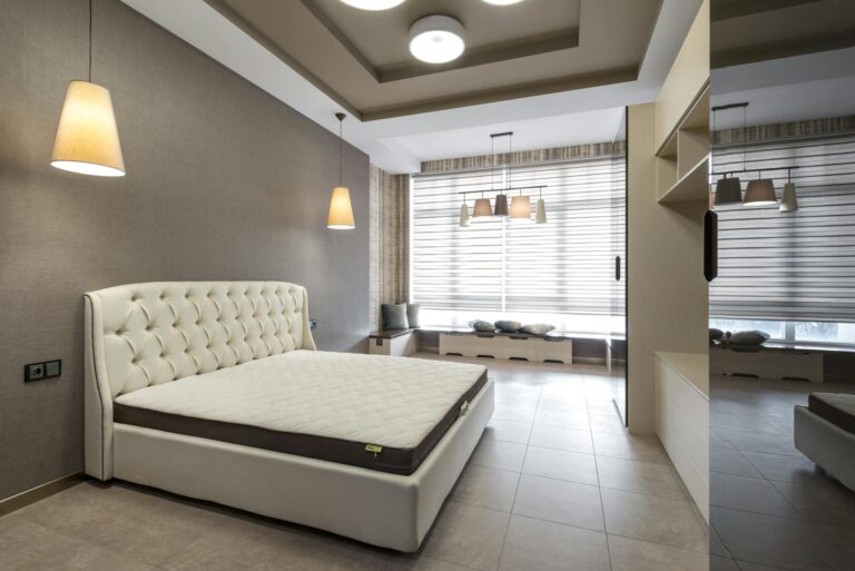 A spacious and modern bedroom featuring a stylish bed, elegant lighting, and large windows for natural light.